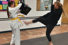 A mother kicks the targets while her daughter holds during a KFMA Family Class. 