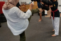 While her daughter holds the targets, Mom works on her front kicks during a KFMA evening family class. While her daughter holds the targets, Mom works on her front kicks during a KFMA evening family class.