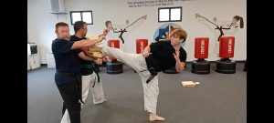 KFMA Black Belt Adult breaking boards with the Reverse Side Kick of Taekwondo.