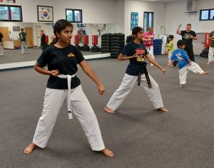 Black Belt Teen assisting in the KFMA Family class working with a White Belt to build confidence through Taekwondo Forms.